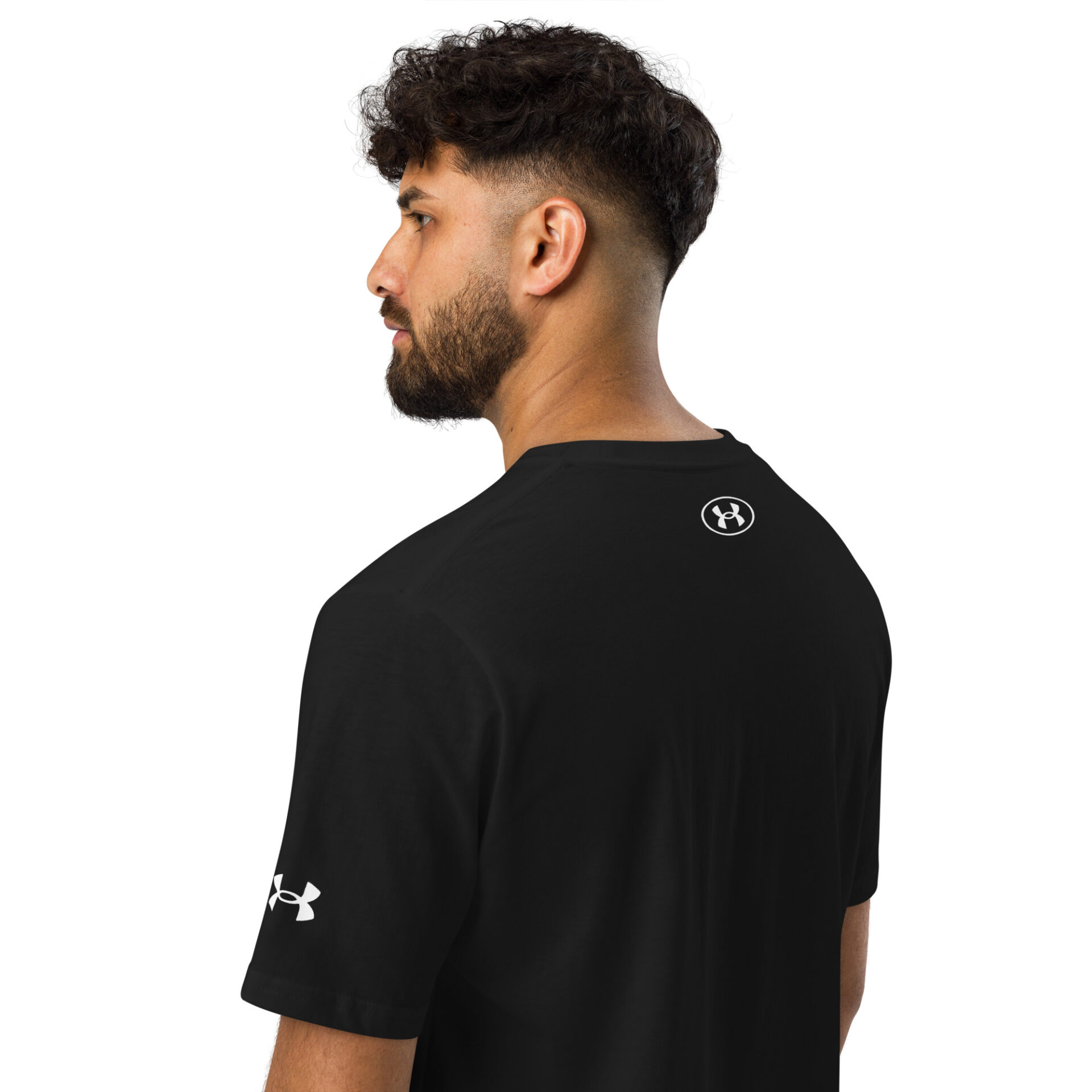 A man with dark curly hair and a beard wears the Under ArmourⓇ athletic t-shirt CHAMP in black, showing the logo on his left sleeve and upper back. He is positioned in a three-quarter view, facing away. A man with dark curly hair and a beard wears the Under ArmourⓇ athletic t-shirt CHAMP in black, showing the logo on his left sleeve and upper back. He is positioned in a three-quarter view, facing away.