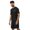 A man with curly hair and a beard wears a black Under ArmourⓇ athletic t-shirt CHAMP and black shorts, standing against a plain white background. A man with curly hair and a beard wears a black Under ArmourⓇ athletic t-shirt CHAMP and black shorts, standing against a plain white background.