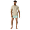 A barefoot man with short curly hair and a beard wears a beige T-shirt and light blue MJL Athletic Shorts featuring a black logo on the left leg, posed against a plain white background. A barefoot man with short curly hair and a beard wears a beige T-shirt and light blue MJL Athletic Shorts featuring a black logo on the left leg, posed against a plain white background.