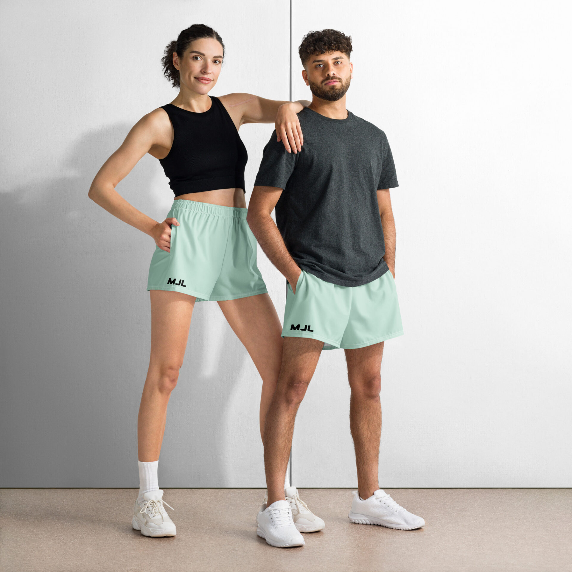 A woman and man pose confidently in mint green MJL Athletic Shorts, white sneakers, and casual tops against a plain background. The woman rests her arm on the mans shoulder, highlighting the stylish sportswear look. A woman and man pose confidently in mint green MJL Athletic Shorts, white sneakers, and casual tops against a plain background. The woman rests her arm on the mans shoulder, highlighting the stylish sportswear look.