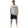 A man with curly hair and a beard wears the Under ArmourⓇ athletic t-shirt embroidered CHAMP, paired with black shorts and white sneakers, standing against a white background. A man with curly hair and a beard wears the Under ArmourⓇ athletic t-shirt embroidered CHAMP, paired with black shorts and white sneakers, standing against a white background.